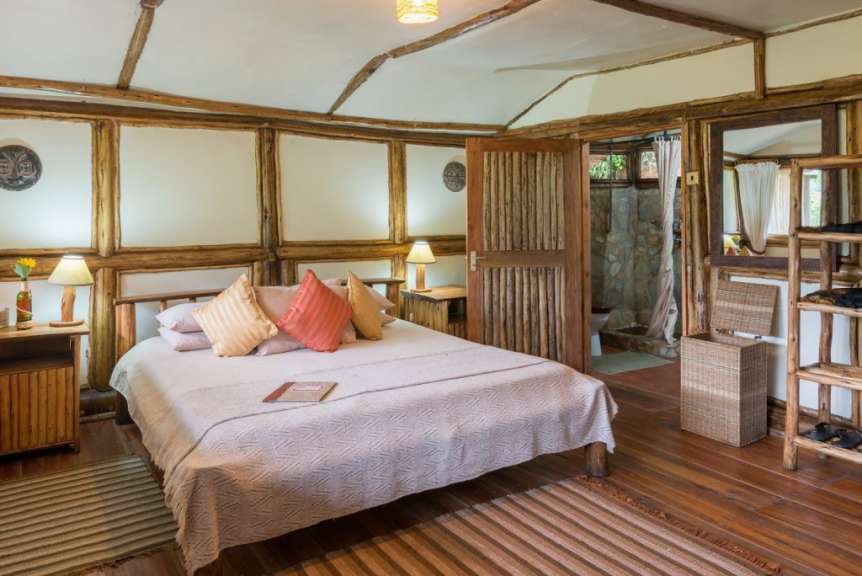 Ein rustikales Schlafzimmer mit Holzelementen, einem Bett mit bunten Kissen und einem offenen Badezimmer.