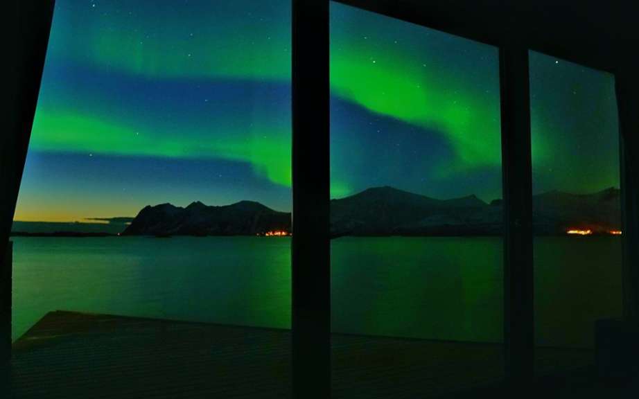Das Nordlicht scheint aus einem Fenster über einen See