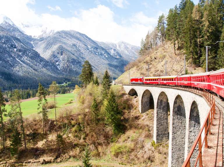 Ein roter Zug fährt auf einer Brücke in den Bergen