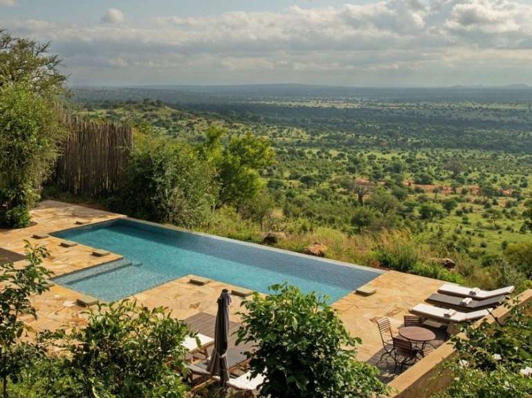 Ein Infinity-Pool auf einer Terrasse mit Blick auf eine weite, grüne Savannenlandschaft.