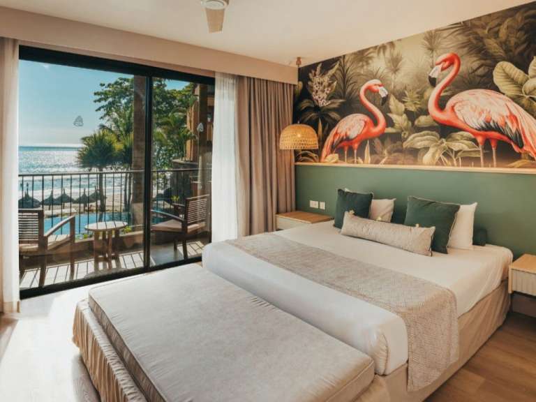 Ein luxuriöses Schlafzimmer mit Blick auf das Meer und den Strand, geschmückt mit Flamingos und tropischen Pflanzen an der Wand.