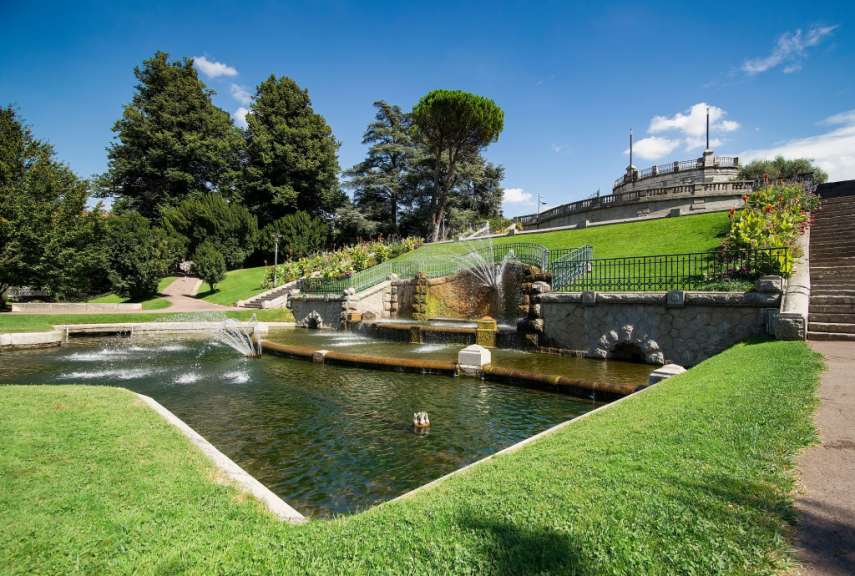 Ein weitläufiger Park mit einem Wasserfall und einem Teich unter blauem Himmel.