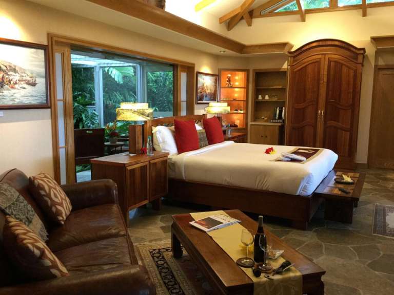 Dieses Bild zeigt ein Schlafzimmer mit einem Bett, einem Sofa, einem Holzkamin und einem großen Fenster, das auf einen Garten hinausgeht.
