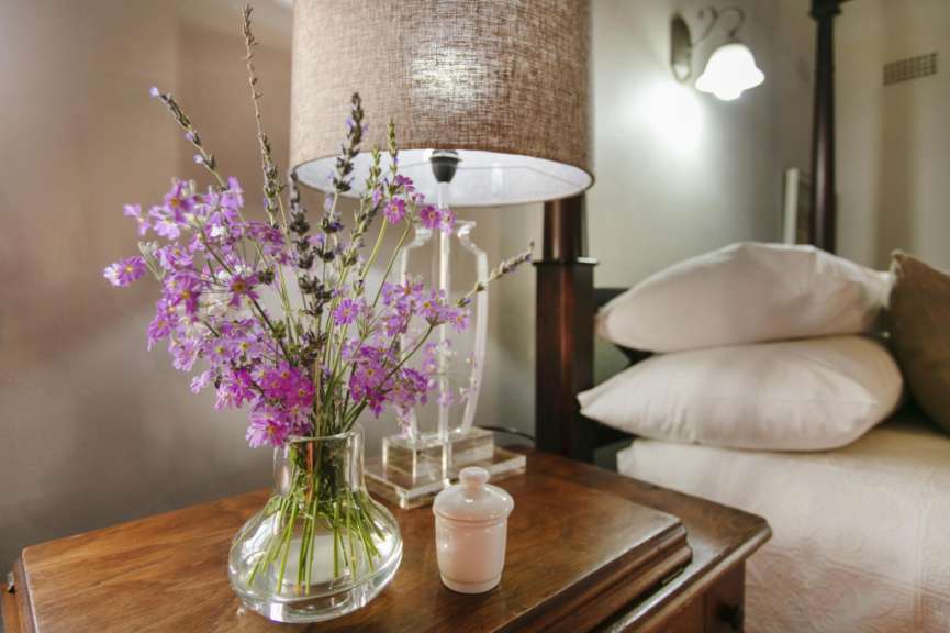 Eine Vase mit lila Blumen sitzt auf einem Nachttisch neben einer Lampe