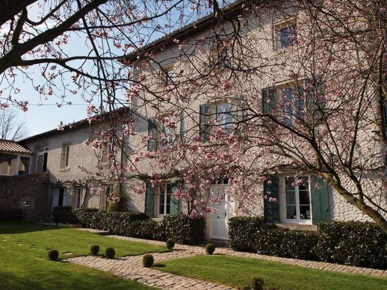 Ein Baum mit rosa Blüten steht vor einem Haus mit grünen Fensterläden