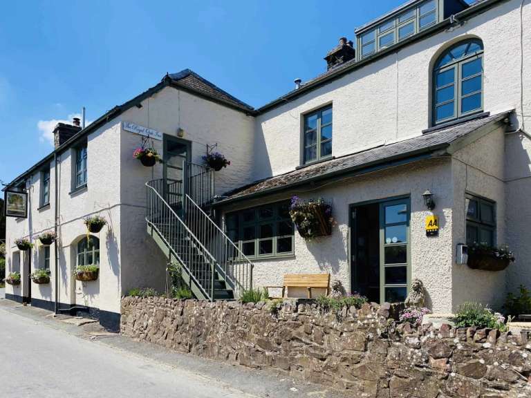 Das Bild zeigt ein weißes Gasthaus mit einem Schild mit der Aufschrift "The Royal Oak Inn" und einem Blumenarrangement, das an der Wand hängt.