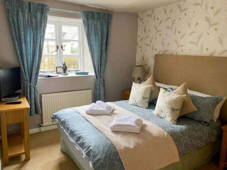 Ein gemütliches Schlafzimmer mit einem Bett, das mit einer hellbeigen Decke und einem gemusterten Tagesdecke bedeckt ist, sowie zwei weiß gefalteten Handtüchern, die auf dem Bett liegen.