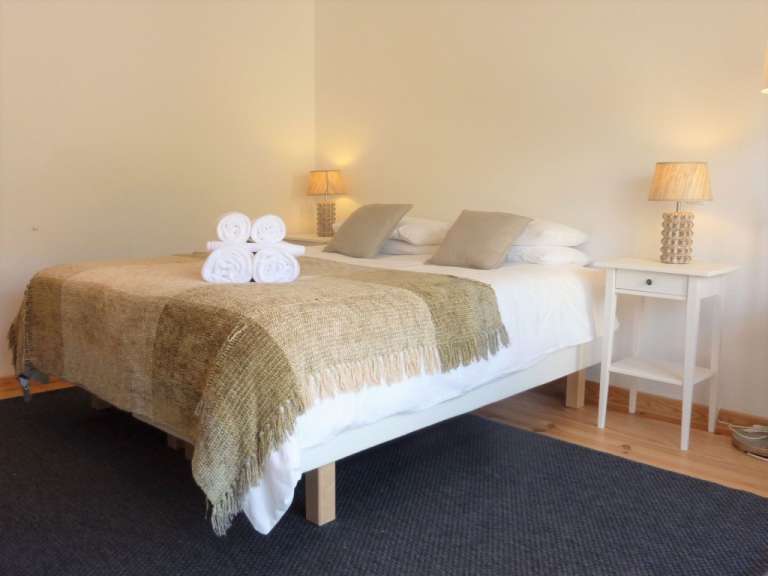 Auf dem Bild ist ein Bett mit einem karierten Überwurf und aufgerollten Handtüchern darauf zu sehen, neben einem Nachttisch mit einer Lampe.