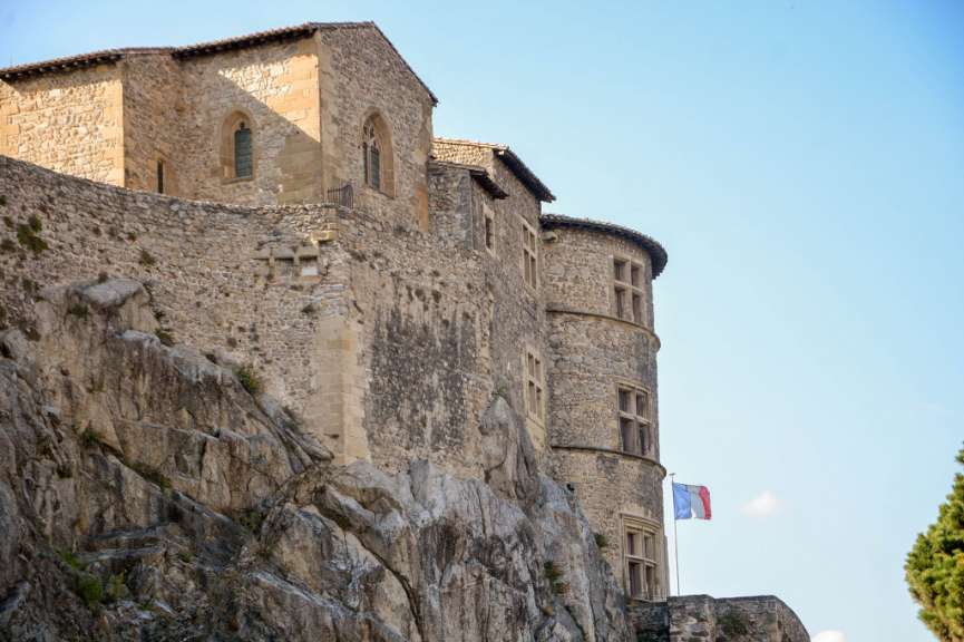 Ein steingemauerter mittelalterlicher Wohnturm auf einem Felsen mit einer französischen Flagge auf der rechten Seite.