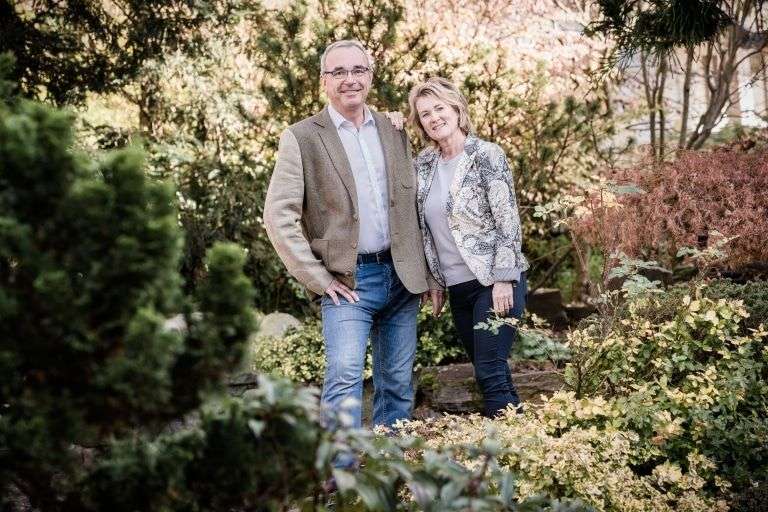 Gastgeber in der Steiermark: Astrid und Peter Ochensberger – ©© Garten Hotel Ochensberger Ein Mann und eine Frau stehen nebeneinander in einem Garten