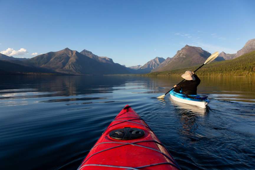 Eine Person paddelt in einem Kajak auf einem See mit Bergen im Hintergrund