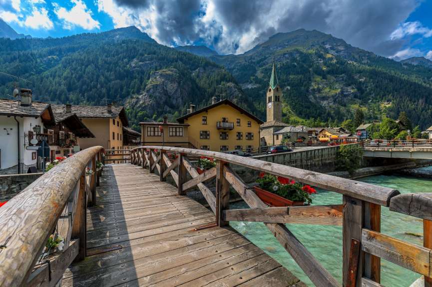 Eine Holzbrücke über einen Fluss in einem Dorf mit Bergen im Hintergrund