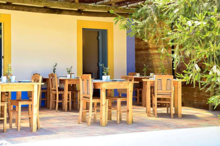 Eine Terrasse mit Holztischen und Stühlen vor einem gelben und blauen Gebäude