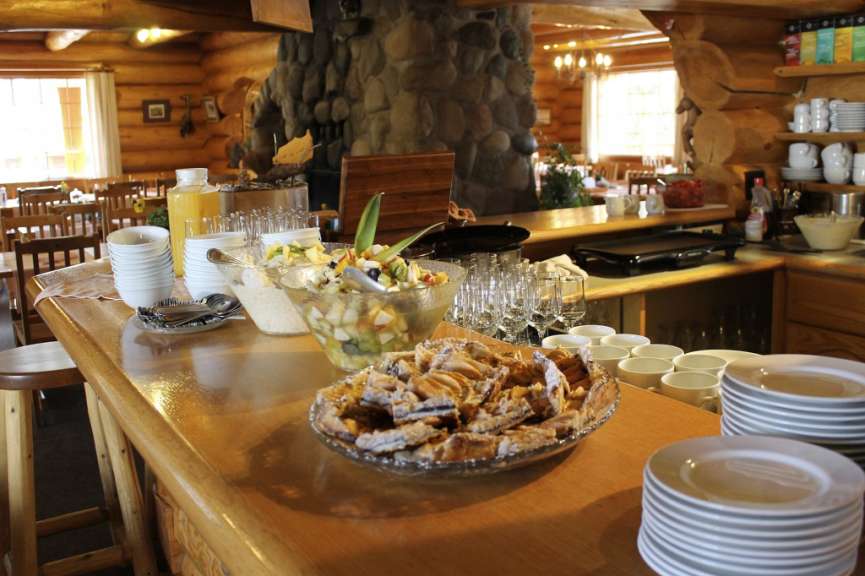 Eine Essensausgabe in einem rustikalen Blockhaus mit Obstsalat, Kuchen und einem Stapel Teller.