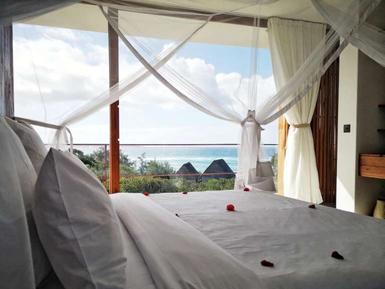 Ein Schlafzimmer mit einem Himmelbett und einem Balkon mit Blick auf den Ozean