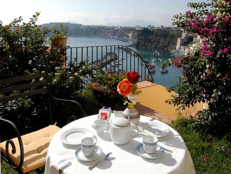 Ein Tisch mit Kaffeetassen und einer Kaffeekanne auf einem Balkon mit Blick auf den Ozean