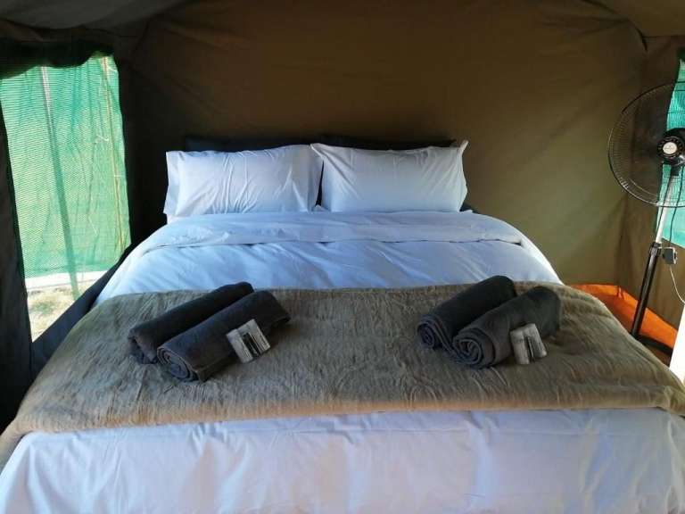 Ein Bett in einem Zelt mit Handtüchern und einem Ventilator