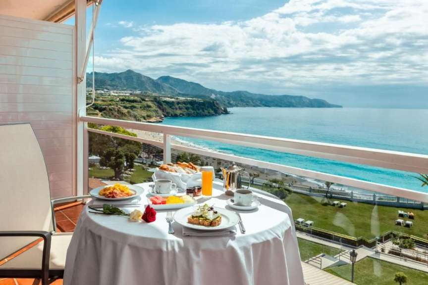 Ein Tisch mit Essen und Getränken auf einem Balkon mit Blick auf den Ozean