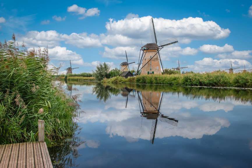 Windmühlen stehen an einem Fluss und spiegeln sich im Wasser