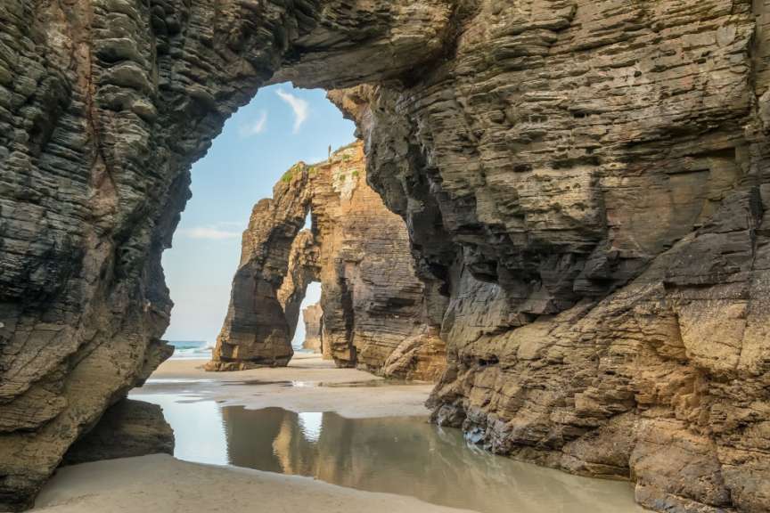 Die Kamera blickt durch zwei Felsbögen am Strand von As Catedrais auf das Meer.