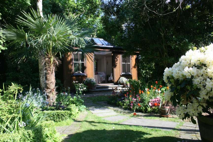 Ein kleines Haus in einem Garten mit Palmen und Blumen