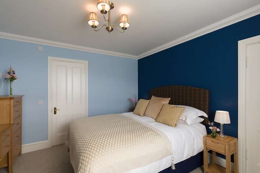 Ein Schlafzimmer mit hellblauen und dunkelblauen Wänden, einem Bett mit gemustertem Überwurf und einem Holznachttisch mit Lampe.