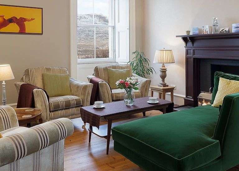 In einem gemütlichen Wohnzimmer stehen Sessel und eine Chaiselongue vor einem Kamin.