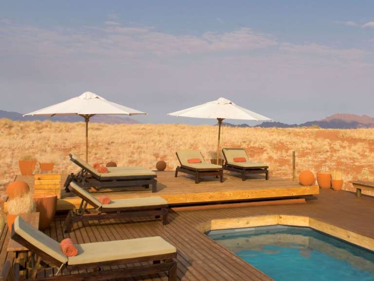 Ein Holzdeck mit Liegestühlen und Sonnenschirmen um einen Pool