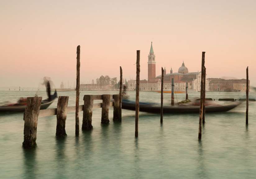 Eine Reihe von Holzpfosten im Wasser mit einer Kirche im Hintergrund
