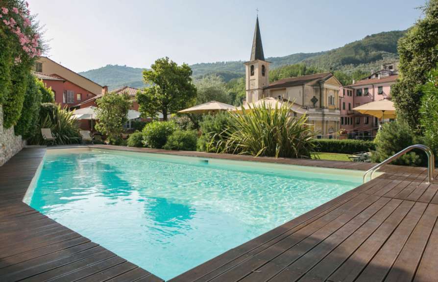 Ein Swimmingpool mit Holzdeck ist vor einer Kulisse von Häusern und einem Kirchturm in der Landschaft gelegen.