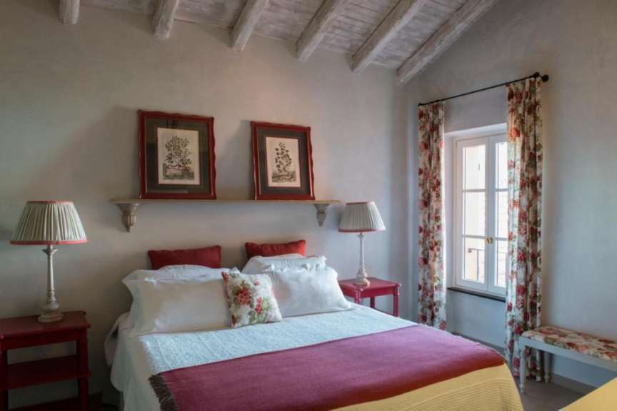 Ein Schlafzimmer mit einem Bett, zwei Nachttischen, einem Fenster mit Vorhängen und einem Regal mit Bildern.