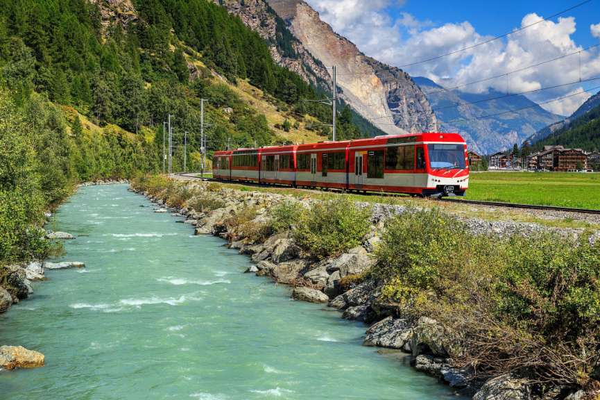 Ein rot-weißer Zug fährt an einem Fluss entlang