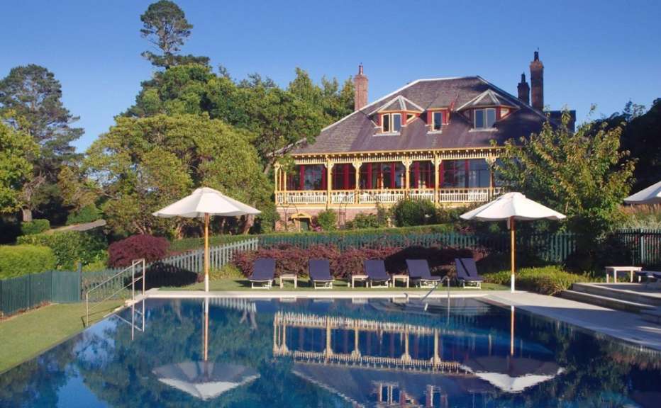 Ein großes Haus mit Veranda und Pool im Vordergrund steht vor einem blauen Himmel.