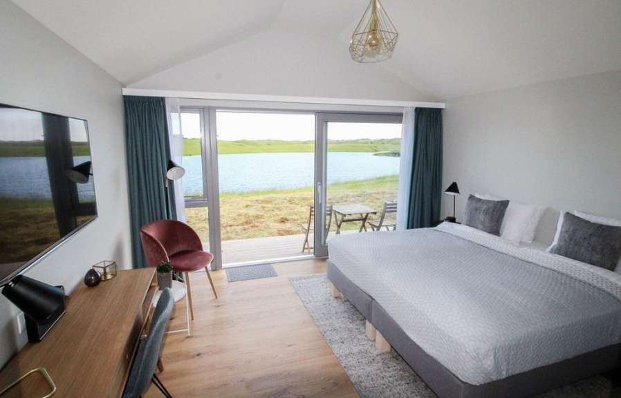 Ein Schlafzimmer mit Blick auf einen See, ausgestattet mit einem Fernseher, einem Schreibtisch, einem bequemen Bett und einem roten Sessel.