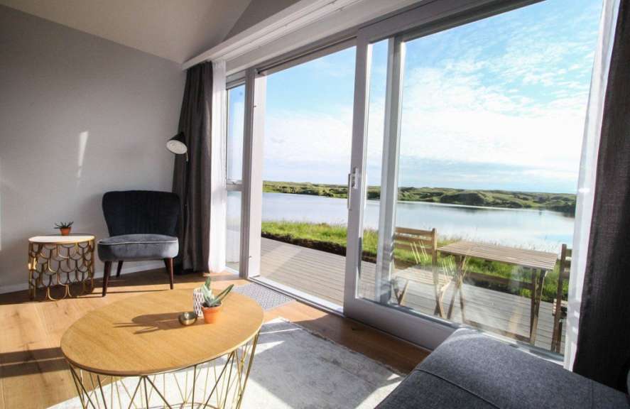 Ein moderner Wohnraum mit großem Fenster und Blick auf einen See mit grünen Hügeln im Hintergrund.
