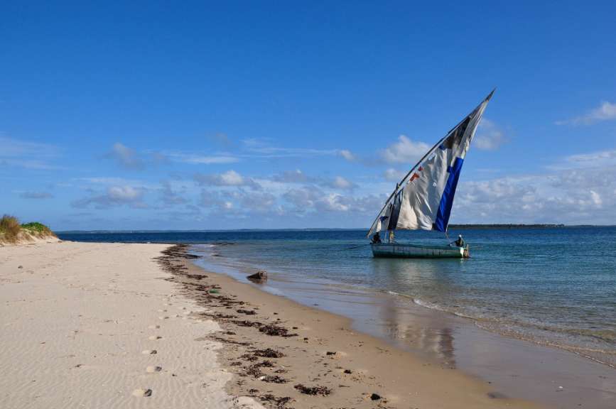 Ein Boot mit einem blauen und weißen Segel schwimmt am Strand