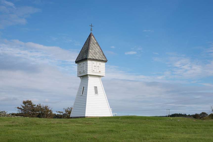Ein weißer Turm mit einer Uhr darauf und einem Kreuz darauf