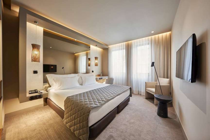 Ein modernes Hotelzimmer mit einem großen Bett, einer Couch, einem Fernseher und großen Fenstern mit Vorhängen.