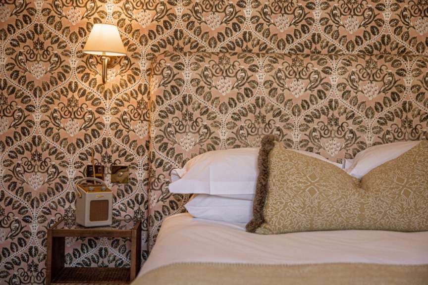 Ein vertikales Bild zeigt ein Bett mit gemusterten Tapeten und Nachttisch.