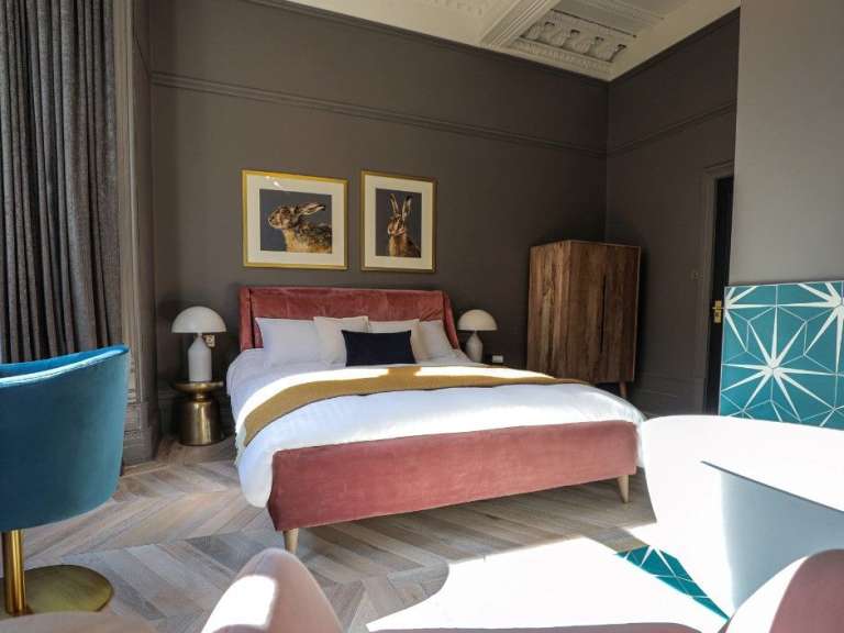 Ein Schlafzimmer mit einem rosafarbenen Bett, zwei Bildern von Hasen an der Wand und einem hölzernen Kleiderschrank.