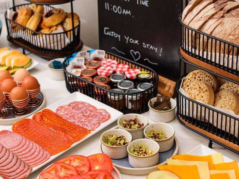Ein reichhaltiges Frühstücksbuffet mit Brot, Gebäck, Wurst, Käse, Obst, Eiern und Marmelade wird serviert.