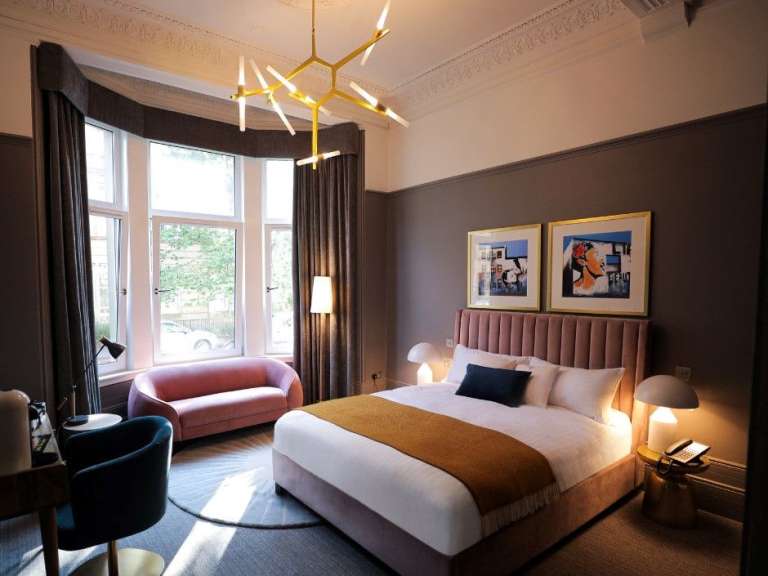 Ein luxuriöses Schlafzimmer mit einem großen Bett, einem rosa Sofa und moderner Kunst an der Wand.