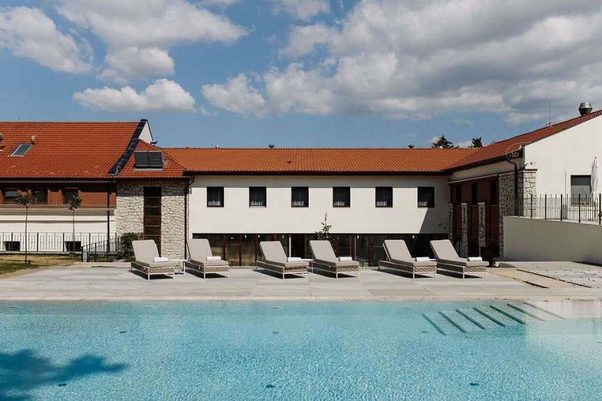 Ein Schwimmbecken und Liegestühle stehen vor einem modernen Gebäude mit Ziegeldach.