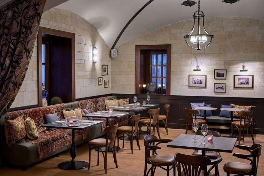 In einem gemütlichen Restaurant mit Steinwänden und gewölbter Decke sind Tische und Stühle aufgestellt, die zu einer entspannten Mahlzeit einladen.