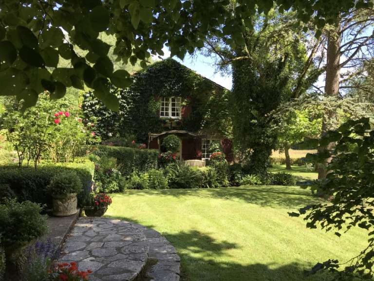 Ein kleines Haus mit roten Fensterläden steht inmitten eines grünen Gartens