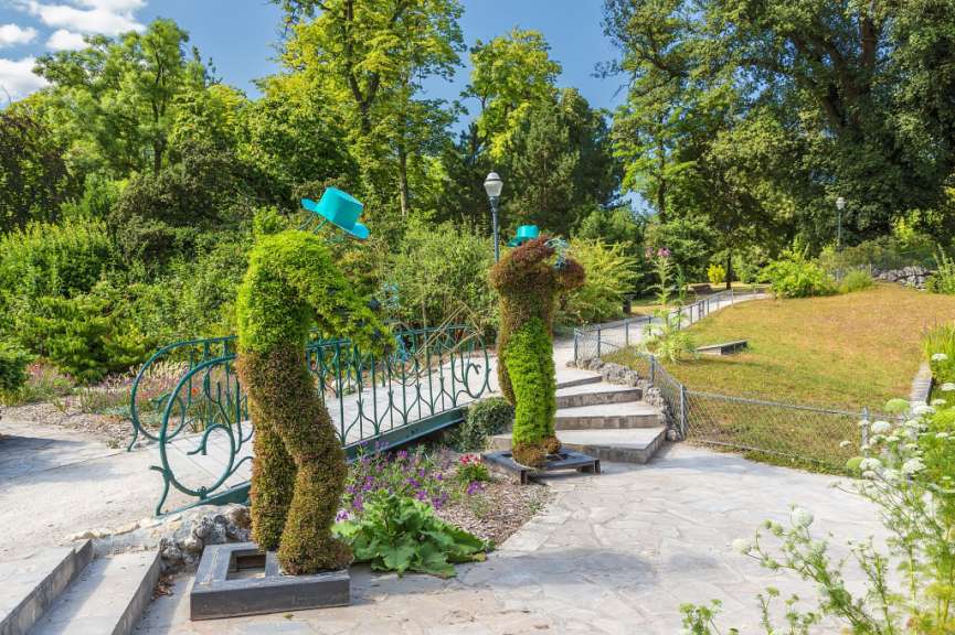 Eine Statue eines Mannes mit blauem Hut steht neben einer Brücke