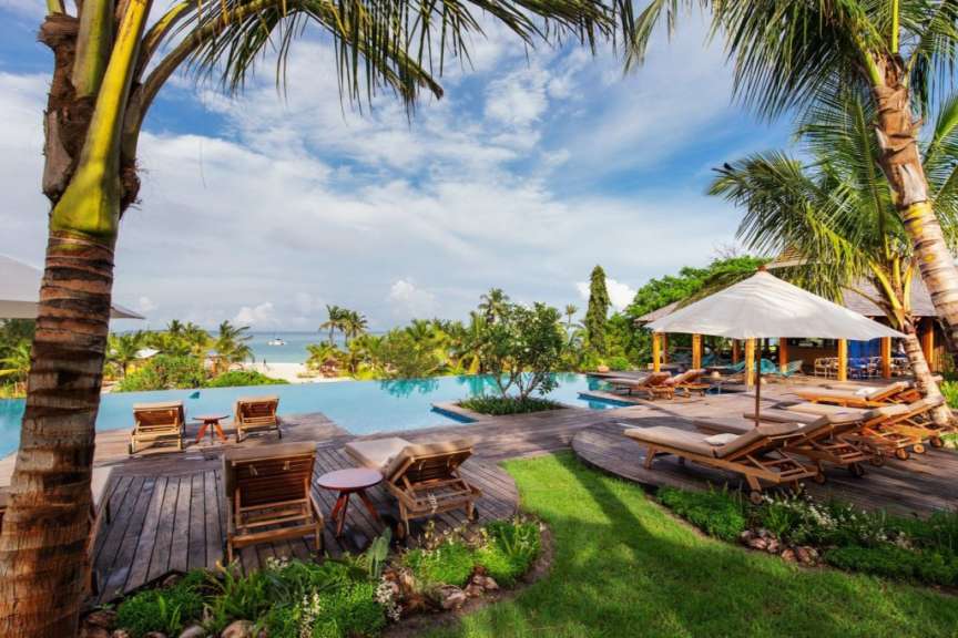 Liegestühle und Sonnenschirme rund um einen Pool mit Blick auf das Meer