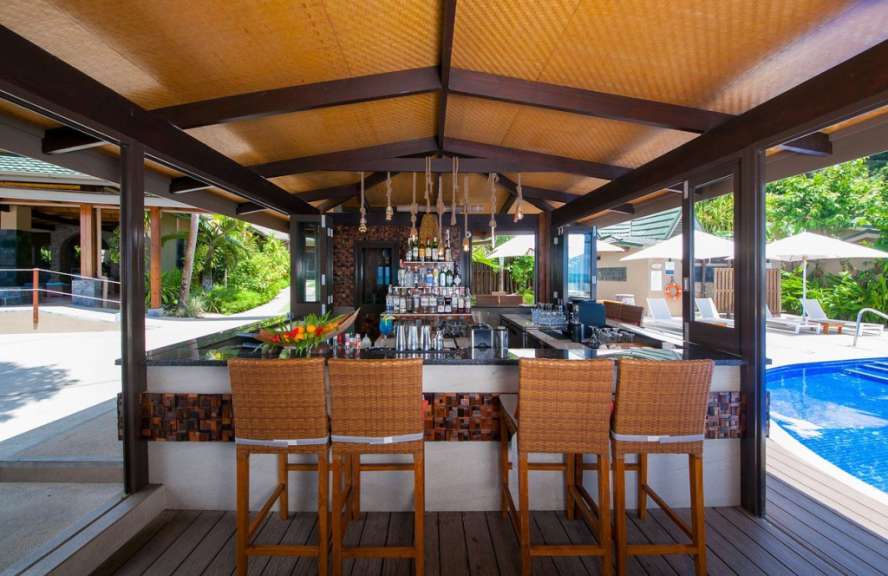 Eine Bar mit Stühlen und Flaschen an der Spitze neben einem Pool