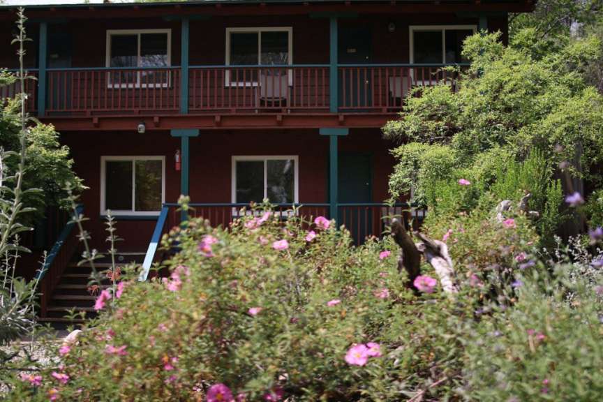 Ein rotes Haus mit einem blauen Balkon und rosa Blumen im Vordergrund