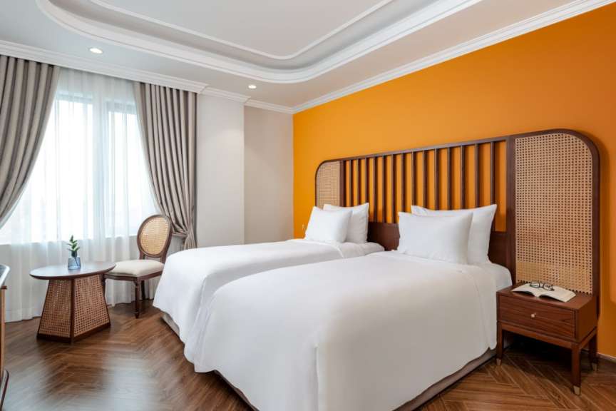 Ein modernes Hotelzimmer mit zwei weißen Betten, einem orangefarbenen Akzent auf der Wand und natürlichen Holzelementen.